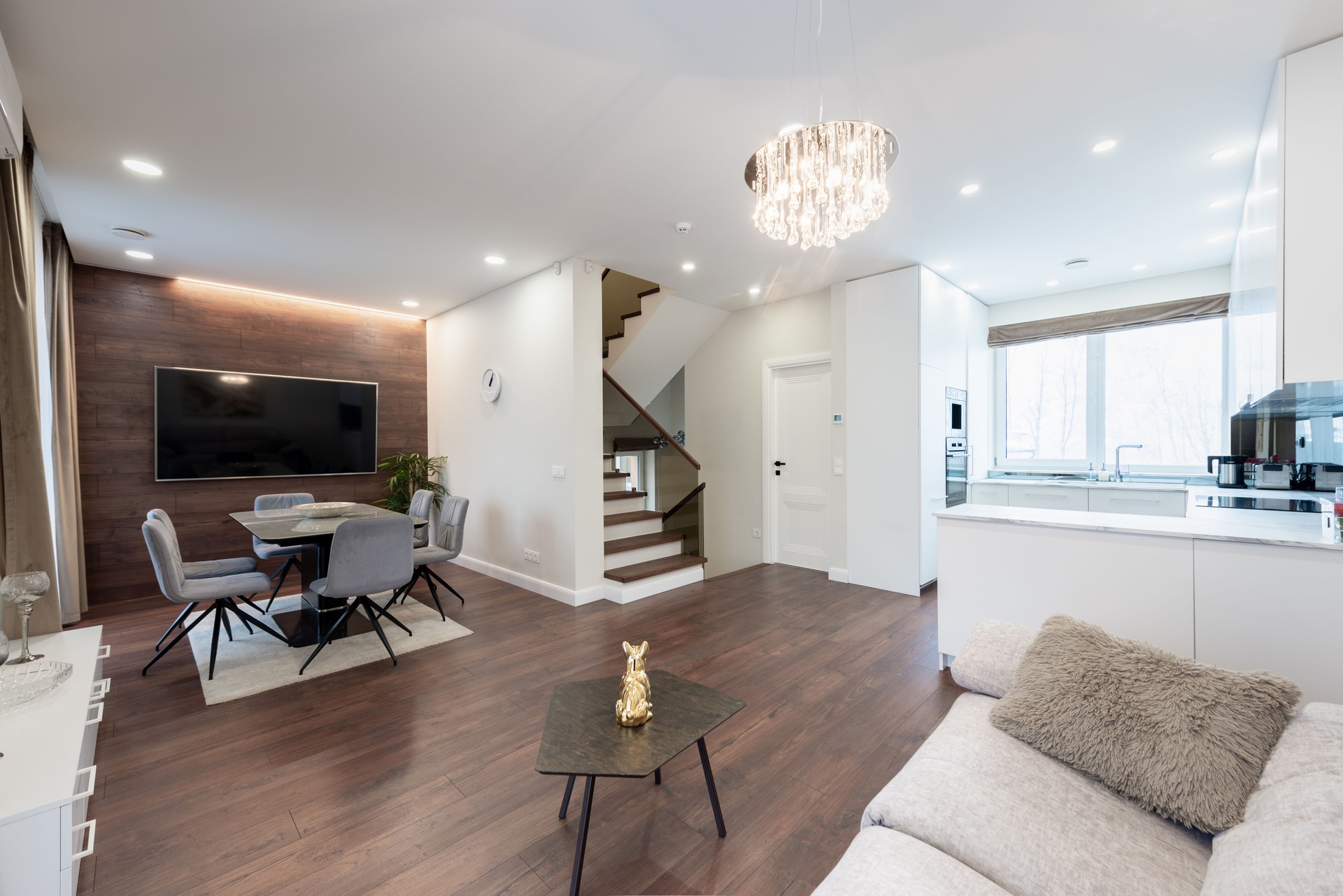 Modern Scadinavian Home Living Room. Luxurious Stylish Modern Apartment. Open Interior, TV Screen and Table with Chairs. Scandinavian Design. Flowers and Curtains. Upstairs and Kitchen in Background